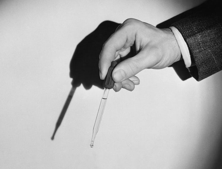 A male hand holding a serum dropper in a black-and-white photo
