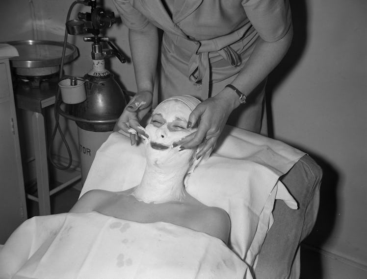 A beautician applying a facial mask to the face of a female client at Helena Rubinstein's London sal...