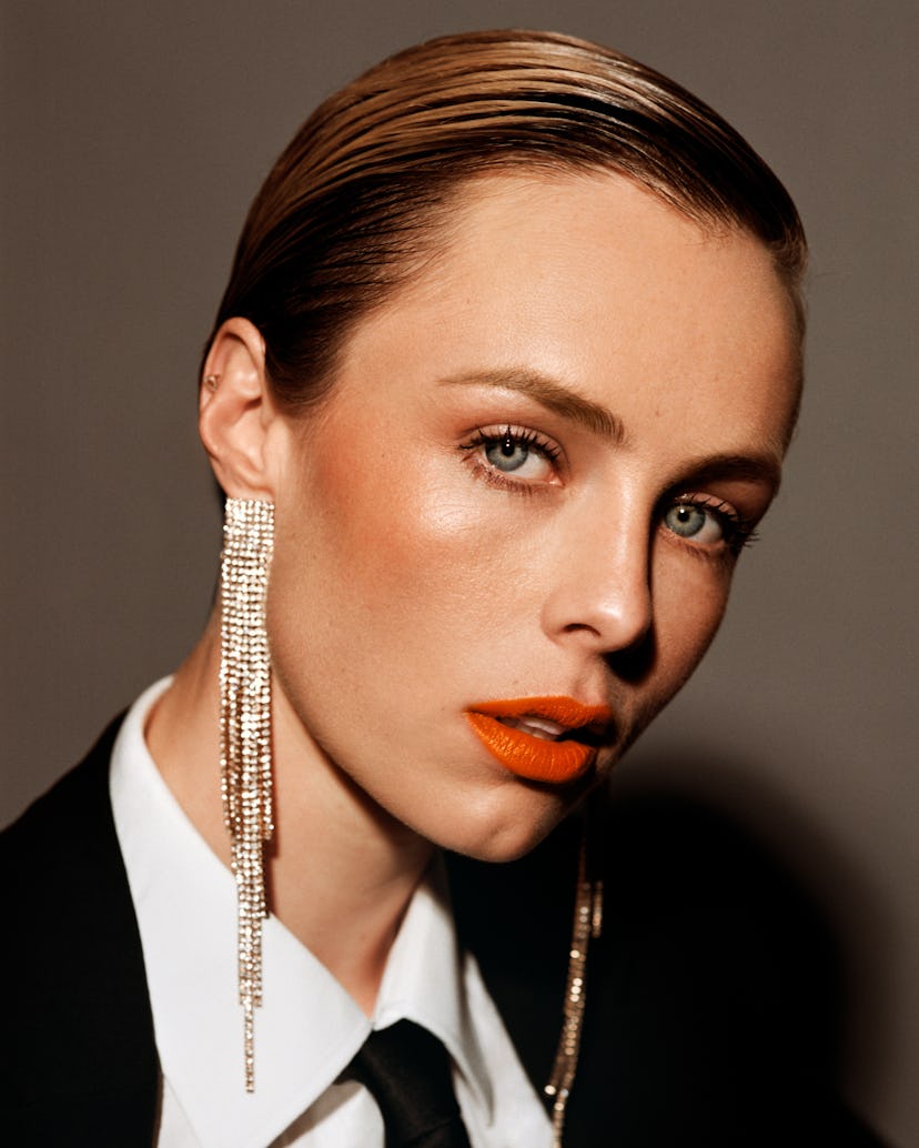 a person with sparkling chandelier earrings, red lipstick, and slicked-back strawberry blonde hair